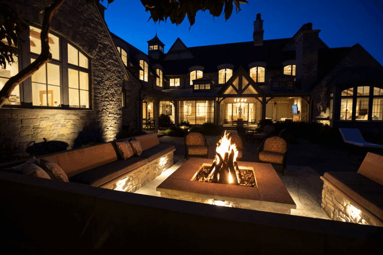 nightime view of large backyard firepit with seating designed by Hursthouse